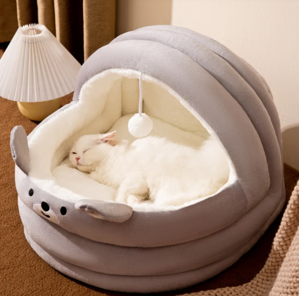 White cat sleeping in a cozy gray plush cat bed with a cute bear design and hanging ball toy