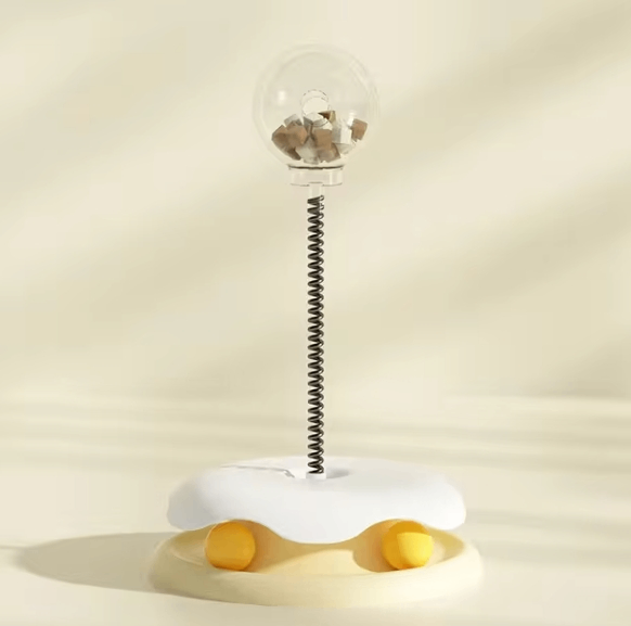 Interactive cat toy with treat dispenser on spring, egg-shaped base, cream background