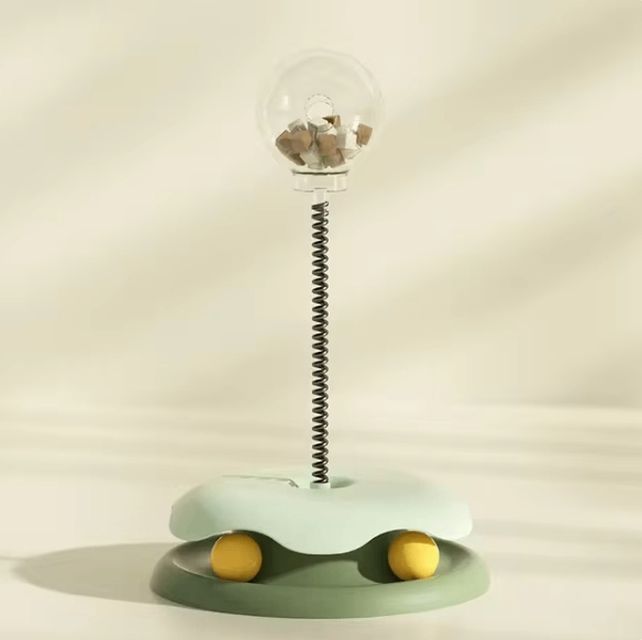 Interactive cat toy with spring rod, clear treat ball, and yellow rolling balls on a green base
