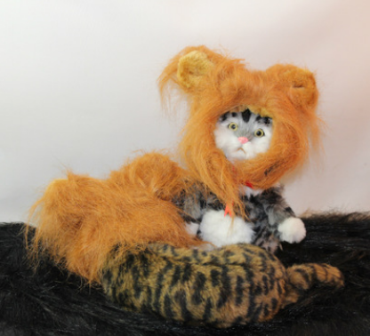 Cat wearing a fluffy lion costume, sitting on a faux fur surface.