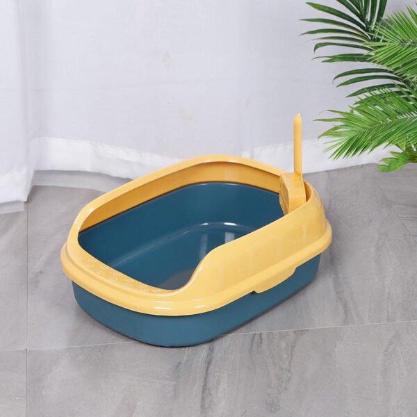 Yellow and blue open cat litter box with scoop, placed on tiled floor near a plant